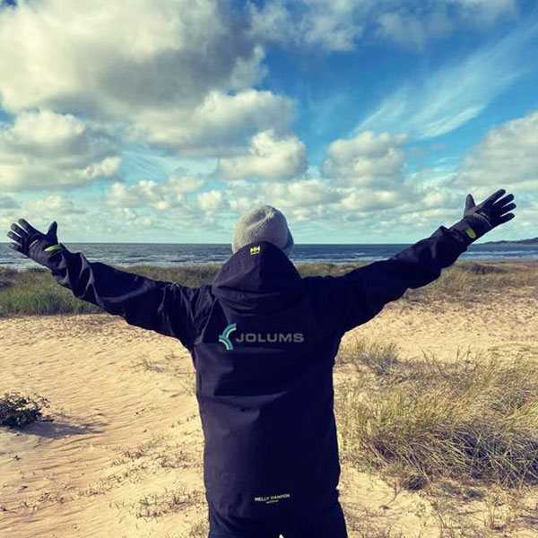 Person på strand med Jolums logga på jackan